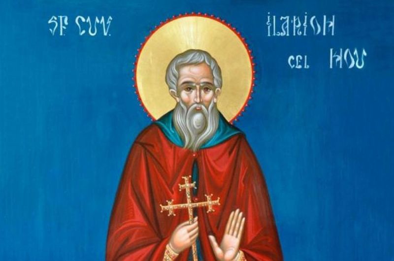 Icoană ortodoxă pe fundal albastru deschis înfățișându-l pe Sfântul Cuvios Ilarion cel Nou de la brâu în sus. Sfântul are barbă și păr cărunte, poartă o mantie roșie peste veșminte monahale verzi-albăstrui, are capul înconjurat de un nimb auriu și ține în mâna dreaptă o cruce aurie cu trei brațe orizontale, în timp ce mâna stângă este ridicată în gest de binecuvântare.
